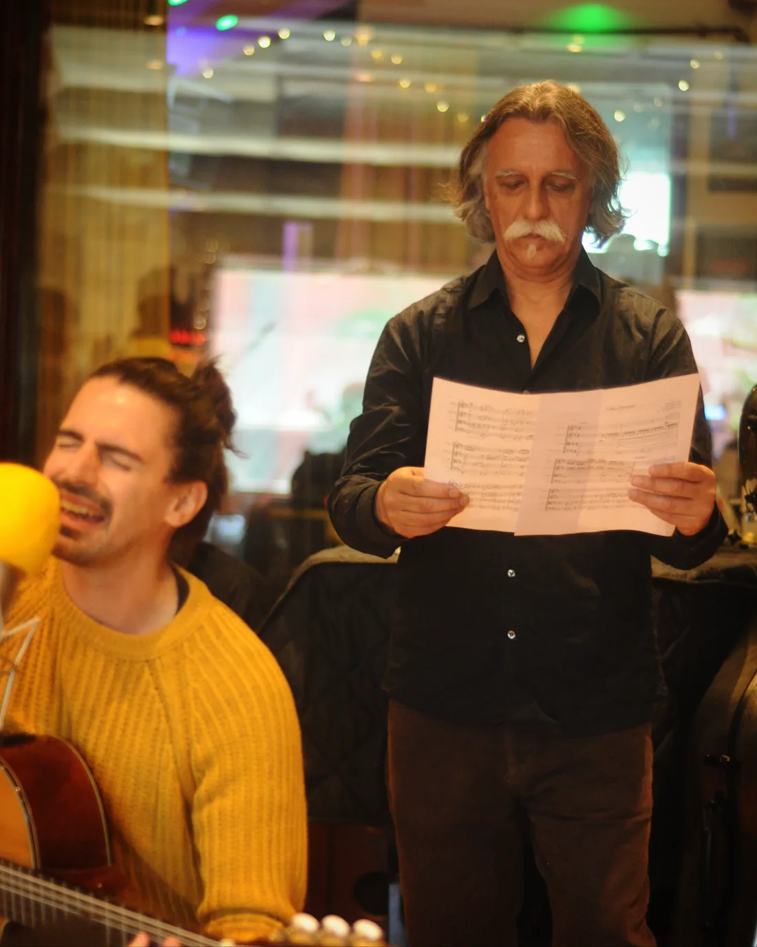 Nahuel Bronzini singing and playing guitar while Teo Bronzini reads the string score